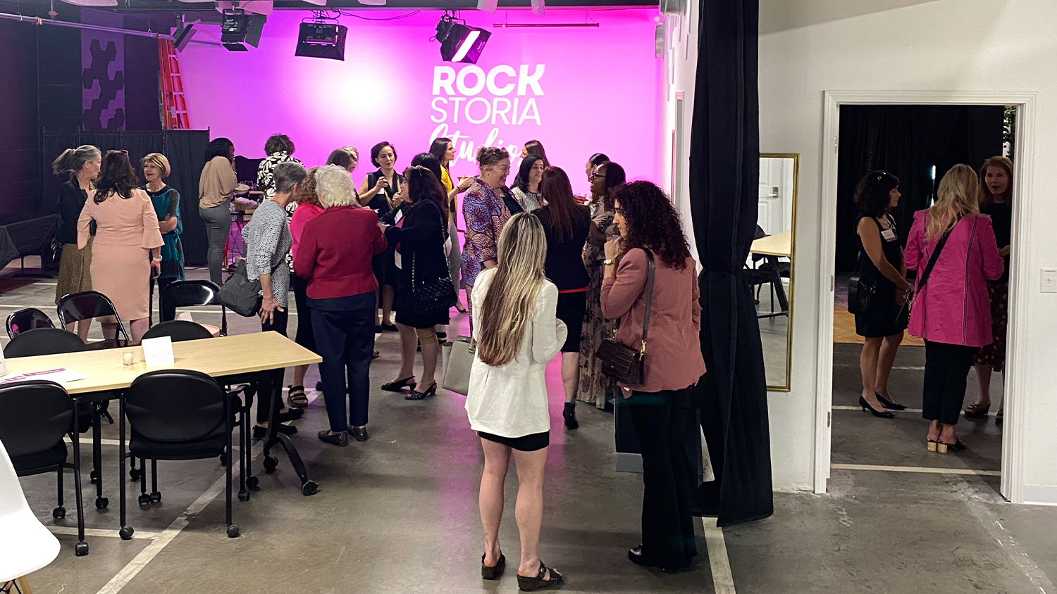NAWBO event rental at Rockstoria Studios in St. Paul, MN. Women mingle in the open concept layout with a wall illuminated in pink light.
