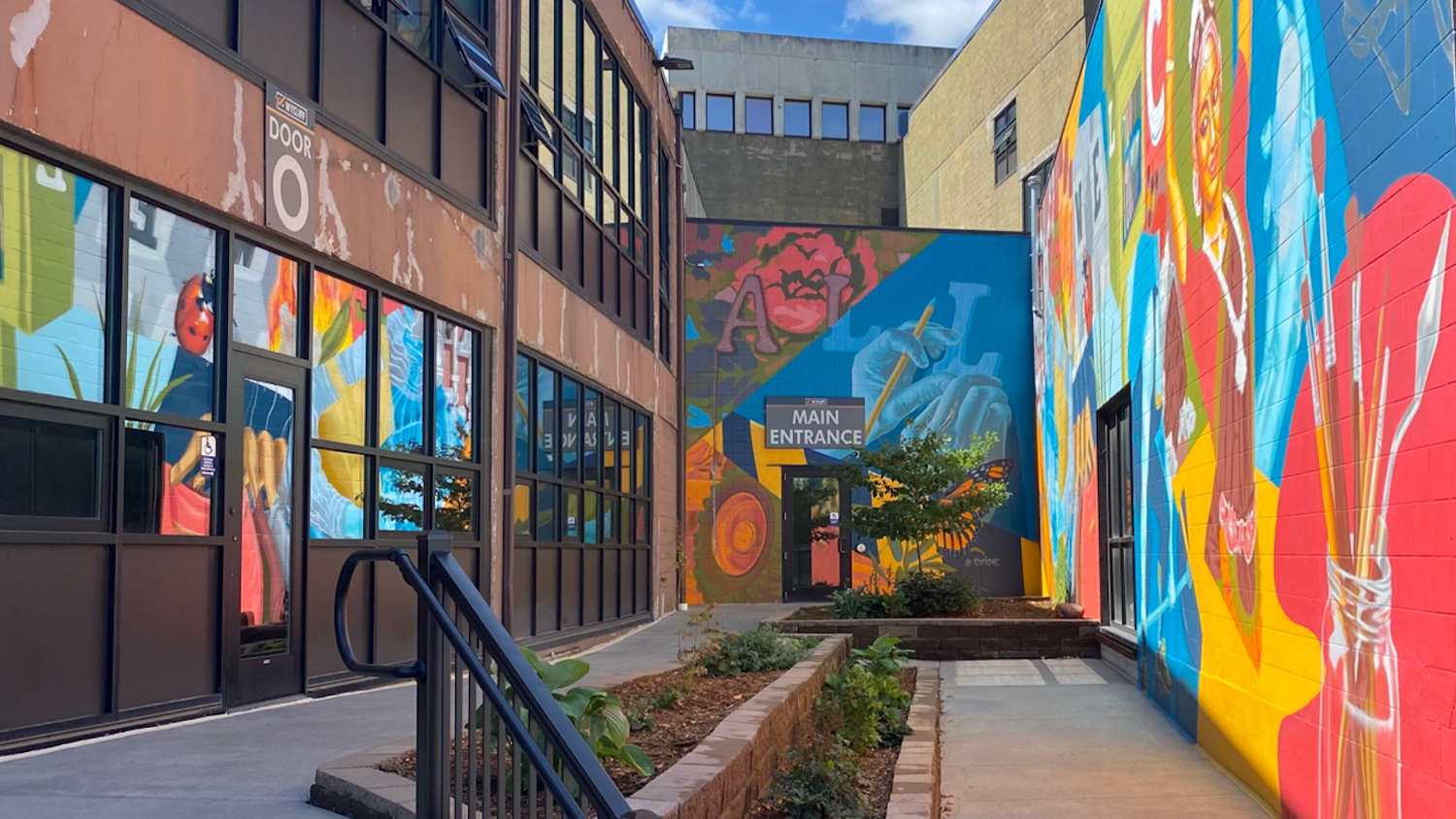 Brick building painted with a colorful mural entrance showing the entry to Rockstoria Studios St. Paul MN located in the WYCLIFF Building on level 3.